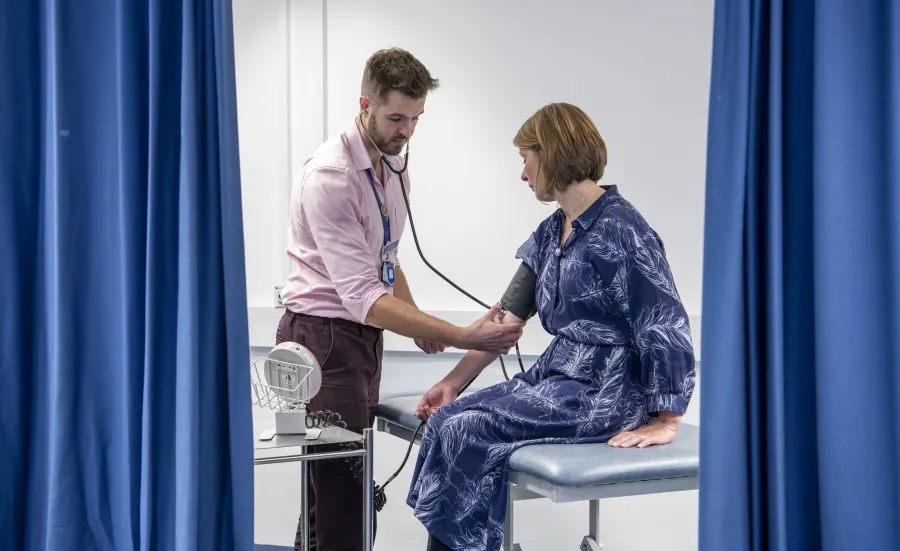 A medicine student examines a patient with a stethoscope in the clinical skills suite
