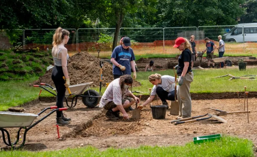 Archaeology students working at an excavation site with wheelbarrows and spades