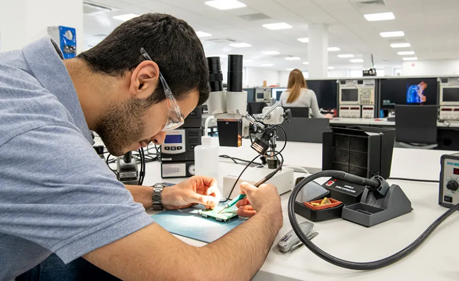 A student applying solder to a PCB at a workbench in the hardware projects lab.