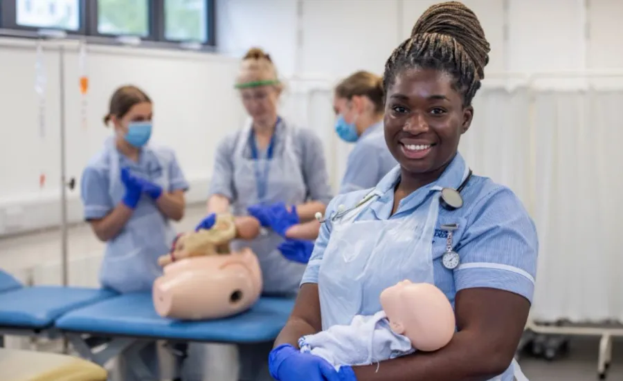A midwifery students hold a baby manikin as students practice their clinical skills