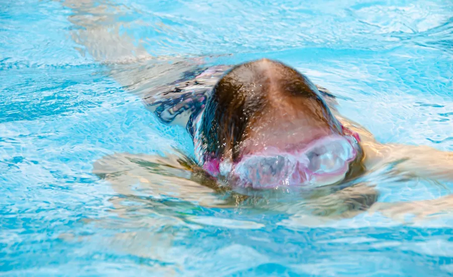 Close up of a child in a swimming pool, their goggles features peeping above the water