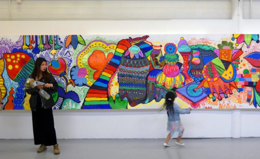 A young child looks at a colourful abstract mural while two adults look on