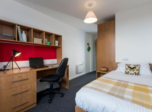 A modern student bedroom with white walls, wooden desk and neatly made double bed.