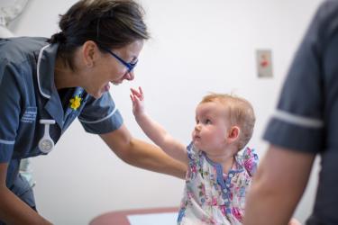 Baby reaches up towards smiling research nurse 