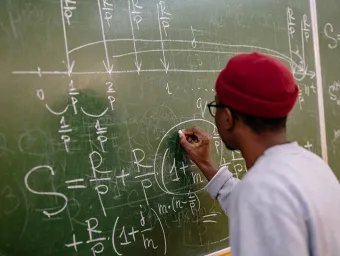 A person with their back to us works out a maths equation on a chalkboard