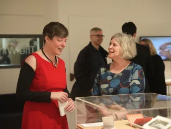 Two guests at a Winchester Gallery event chat next to an exhibit in a glass case. Other guests chat in the background.