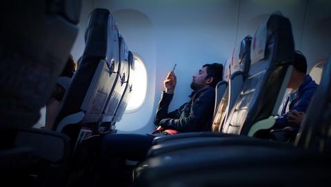 A man looks at his mobile phone while seated on a plane flight