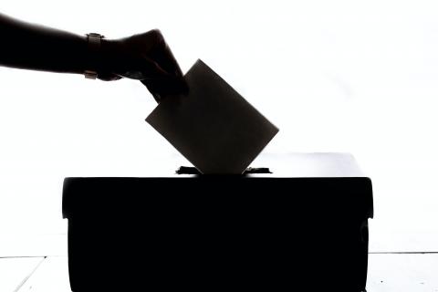 A silhouette of somebody's hand placing their vote into the polling booth box
