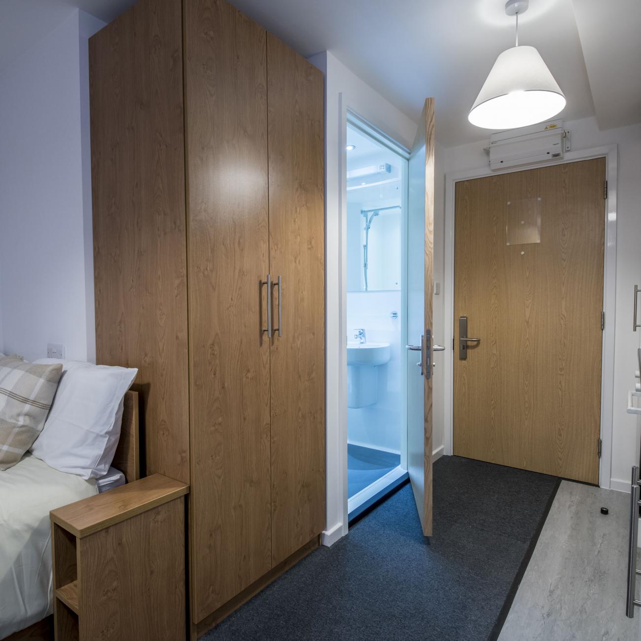 A modern studio flat showing bed, kitchenette and entrance to bathroom.