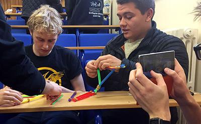 Student using a phone to shoot a video of two other students conducting an experiment
