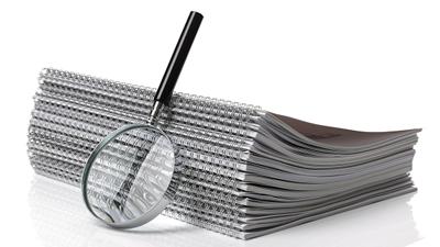 Image of reports stacked in a pile with a magnifying glass