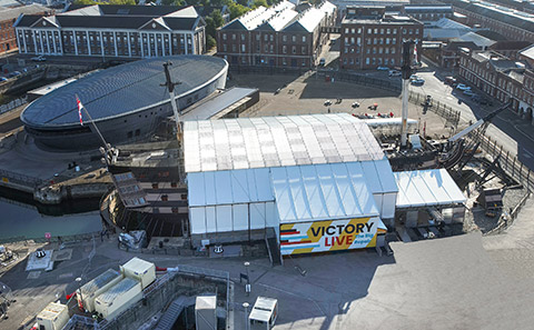 Historic ship HMS Victory see from above and covered by scaffolding roof with bow and stern protruding.