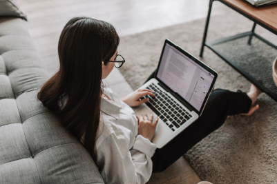 A student using their laptop when sat in front of their sofa.