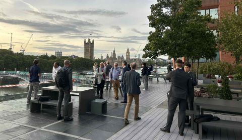 People networking on a London terrace overlooking the River Thames and the Palace of Westminster.