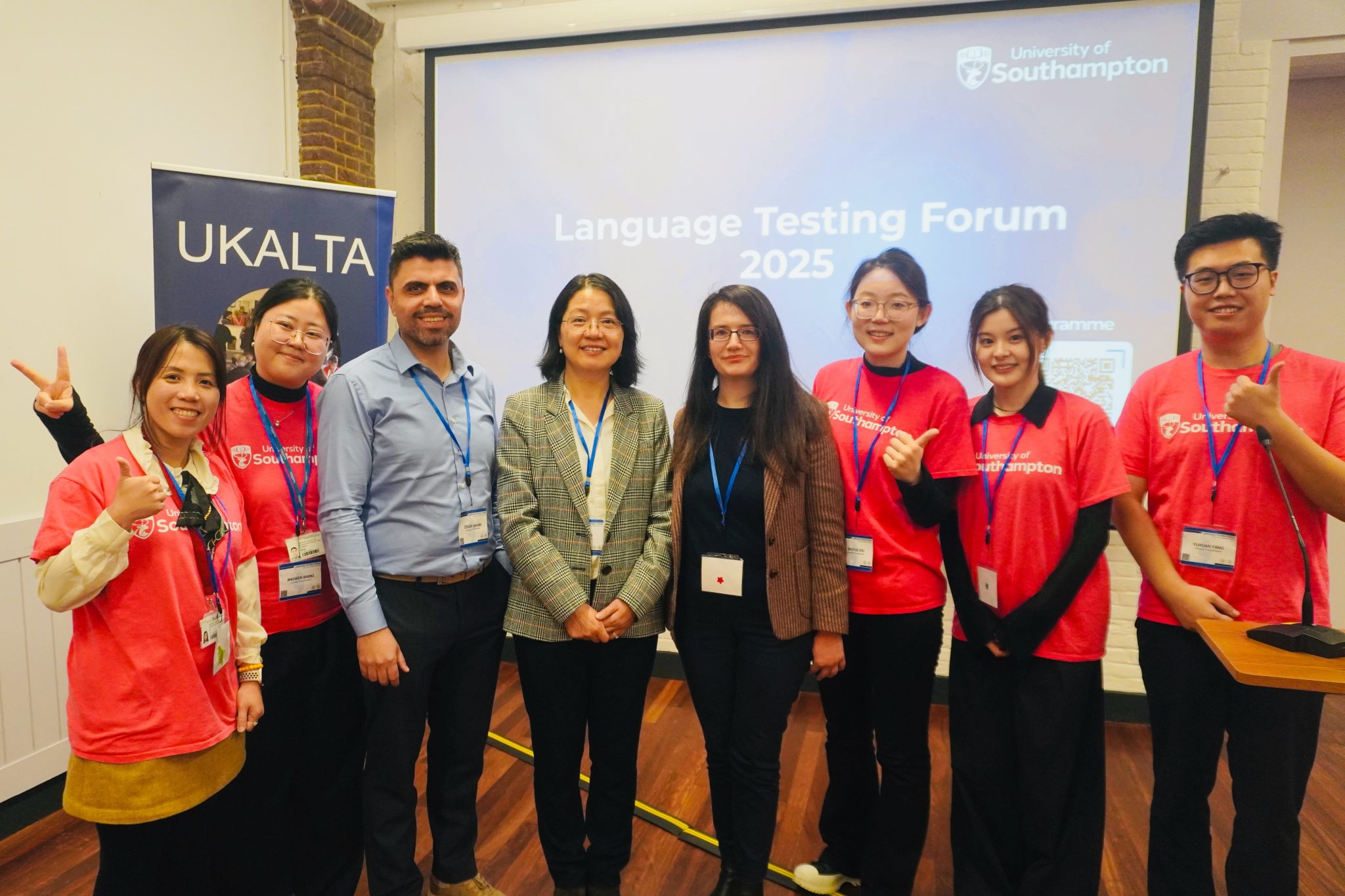 A group of people stands in front of a presentation screen that reads “Language Testing Forum 2025,” with a UKALTA banner on the left. Several individuals are wearing bright pink T-shirts with the University of Southampton logo.