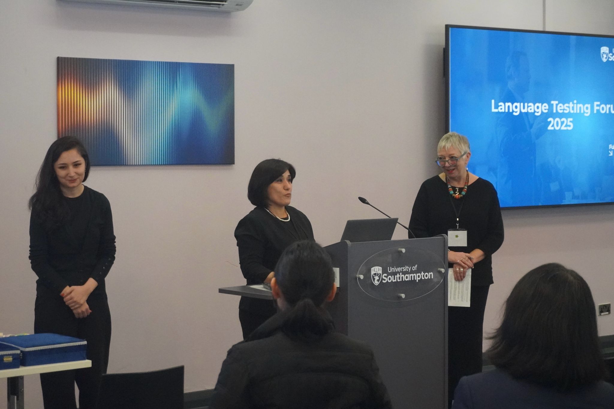 Three individuals stand near a podium with a University of Southampton logo, while a screen in the background shows “Language Testing Forum 2025.”