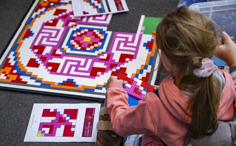 A child sat on the floor making a Lego mosaic out of purple, white and blue bricks.