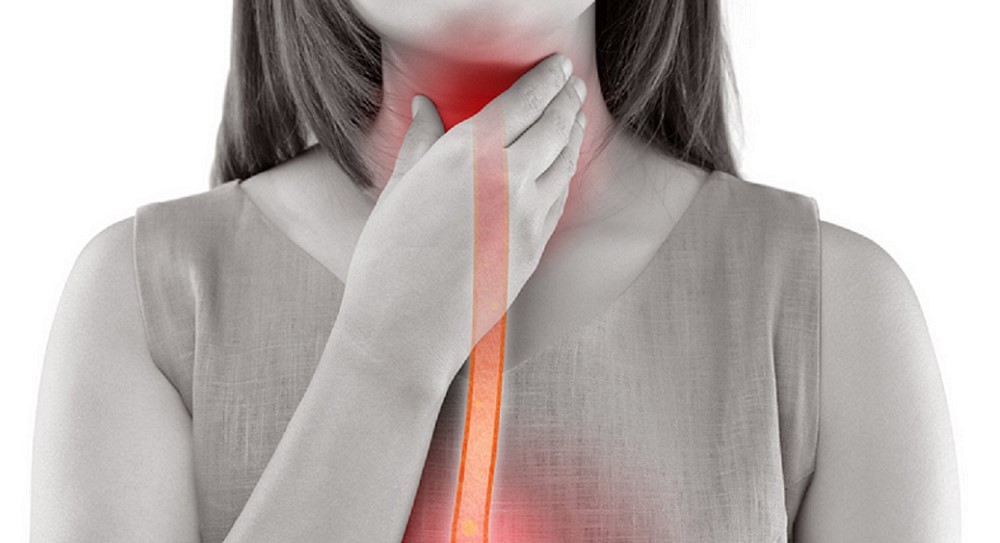 A grayscale depiction of a woman touching her throat with one hand, symbolising discomfort, or pain in that area. A bright red and orange gradient highlights her esophagus, from the throat to the upper chest, suggesting inflammation or a medical condition affecting such as acid reflux, swallowing difficulties, or another issue.