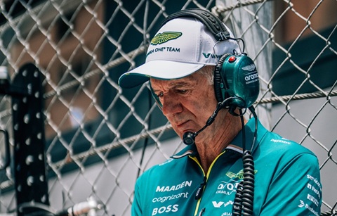 A man wearing a white cap, large headphones and teal T-shirt is looking down
