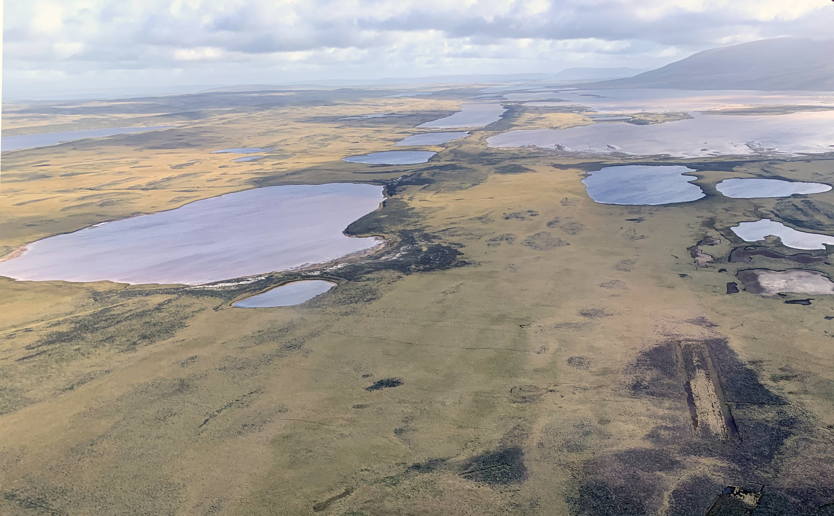 A view from the air showing a green treeless moorland landscape with several bodies of water and a mountain in the far distance.