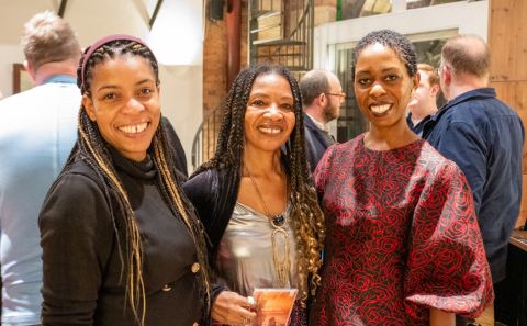 Three women stand next to eachother smiling looking at the camera