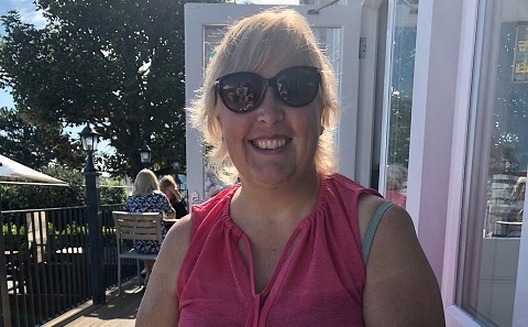 A smiling woman in a pink top sitting in the sunshine