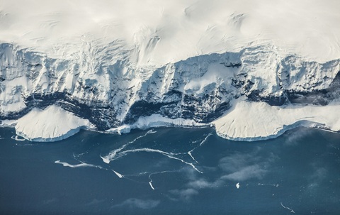 Aerial view of snowy cliffs meeting blue sea water