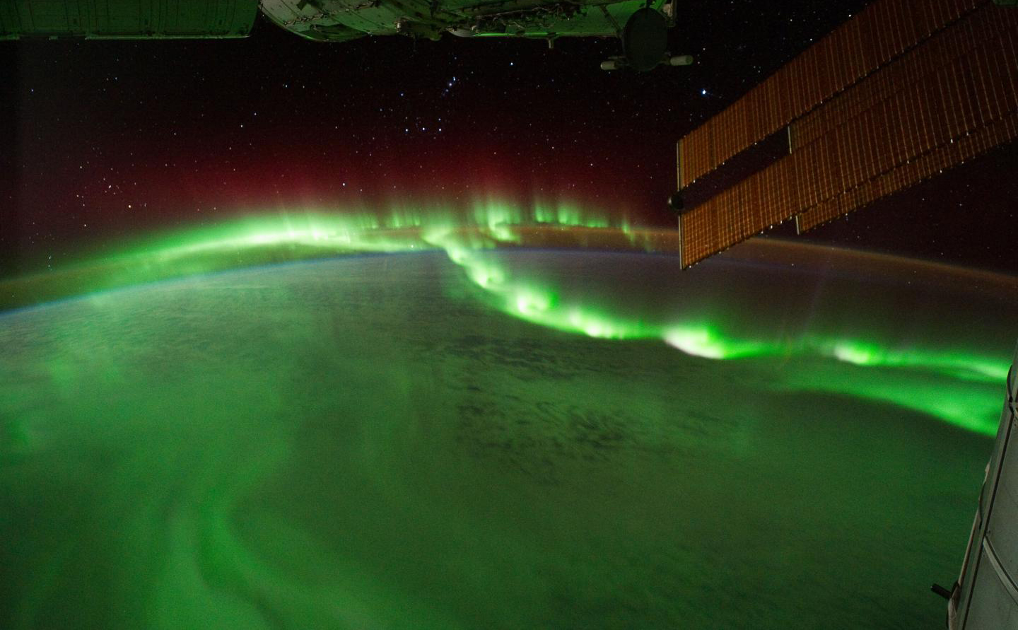 Earth seen from space with a green auroral display blanketing the sky above the planet.