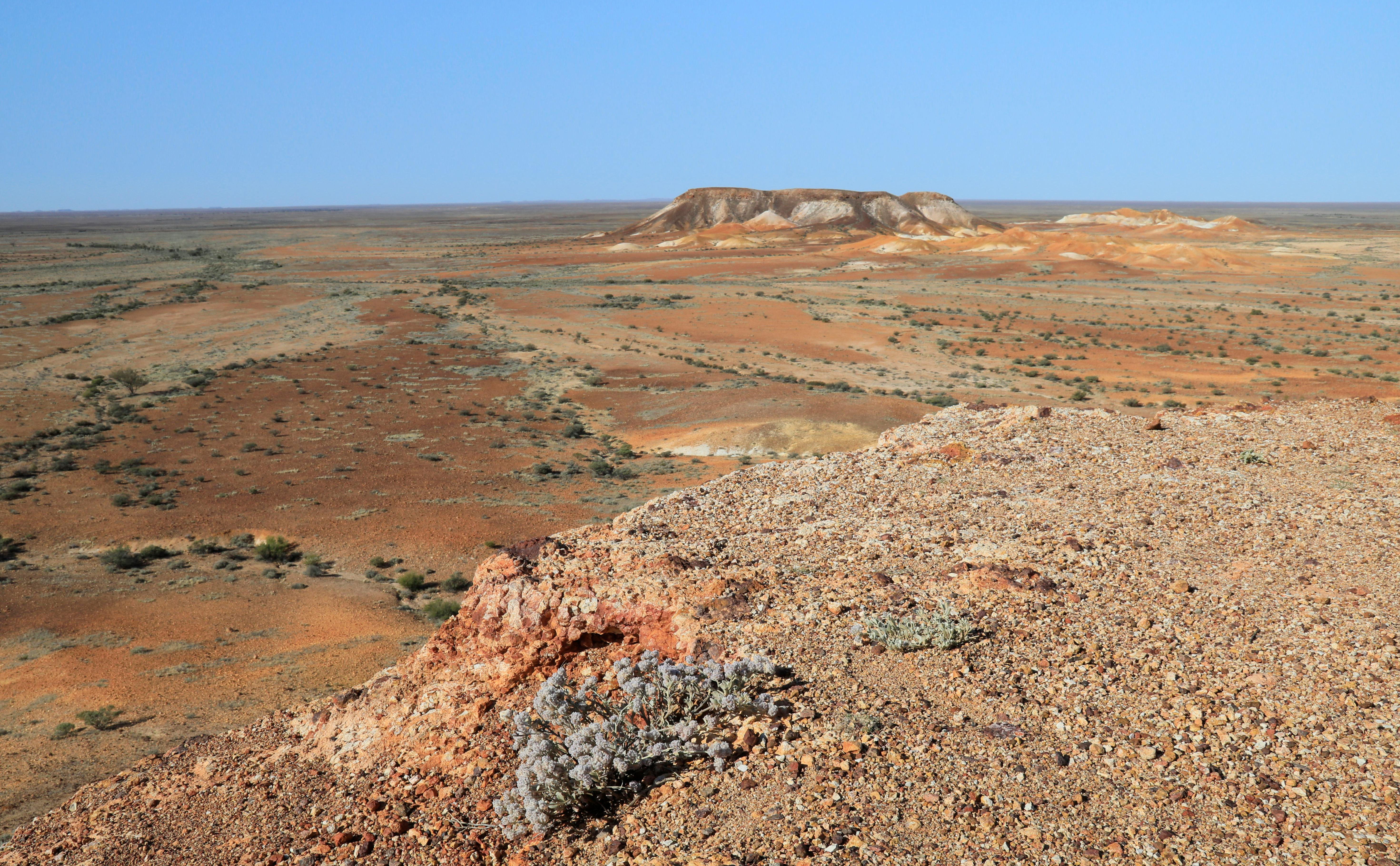 A dry desert landscape with a rocky hill in the foreground, a dry plain behind and another rocky hill in the distance.