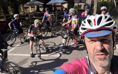 A man wearing a cycle helmet in the foreground, with a group of cyclists on their bikes in the background