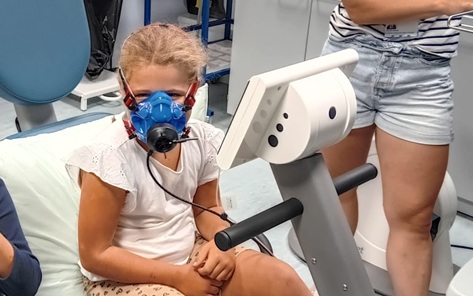 Young girl wearing a blue breathing mask sitting on an exercise bike
