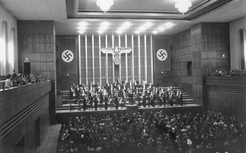 Black and white photo of a concert hall with an orchestra on the stage and a large audience