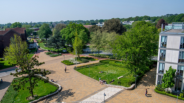 Overhead view of Southampton's leafy Highfield Campus. The view shows students walking and sitting along a tree lined path towards a red brick building.