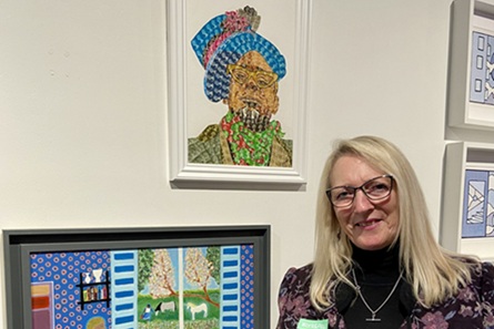 A woman with long hair and glasses standing in front of framed artwork hanging on a white wall