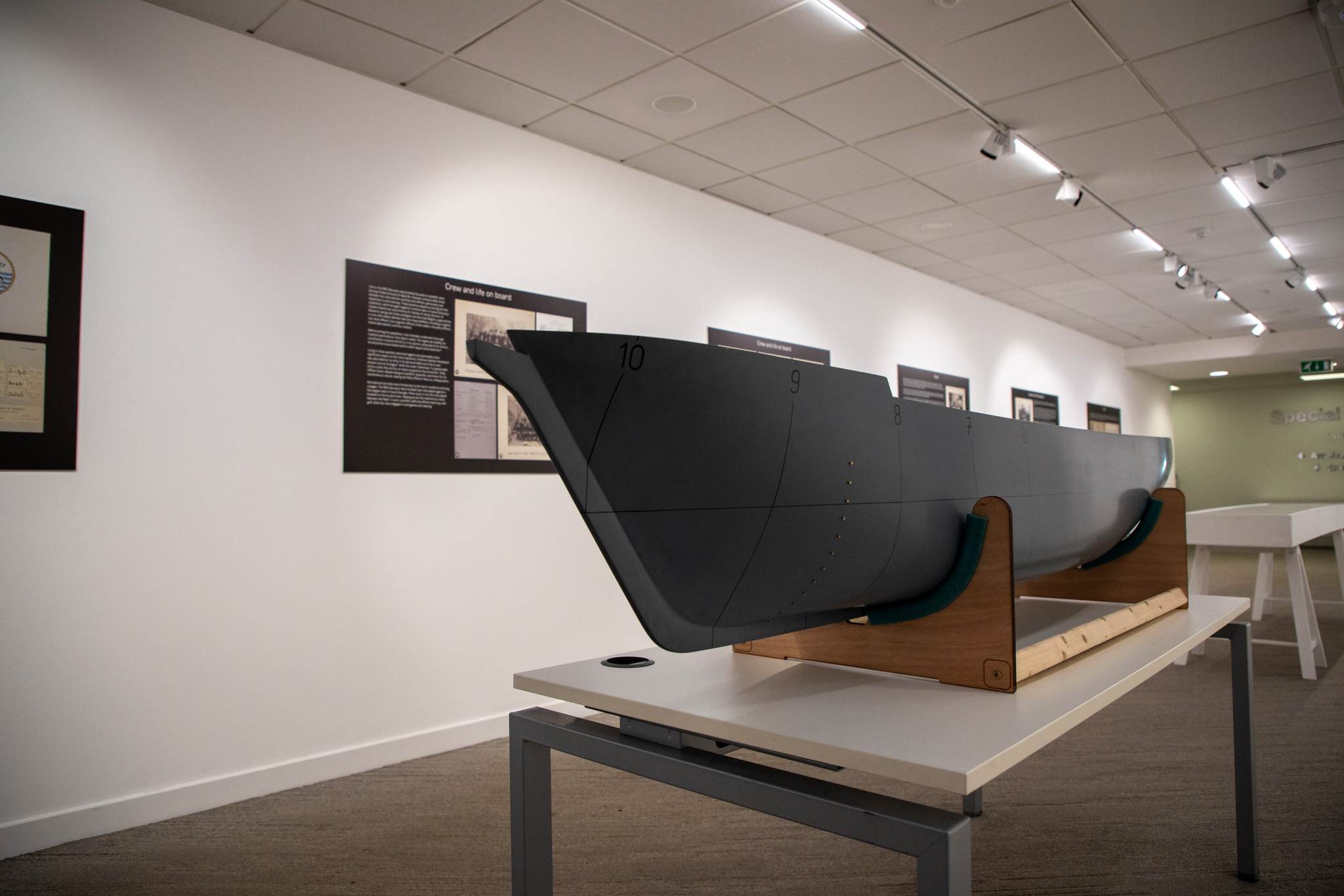 A model ship hull on a white table, with wall displays in the background.