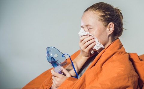 A woman holding a nebuliser and struggling to breath