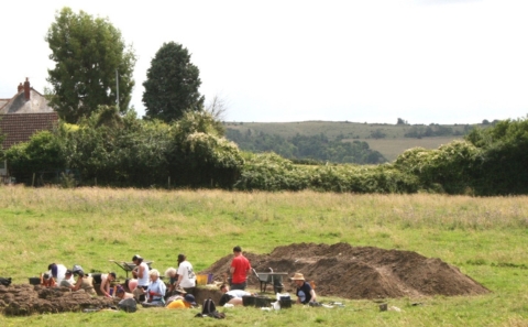 Multiple people are shown in a field working on an excavation