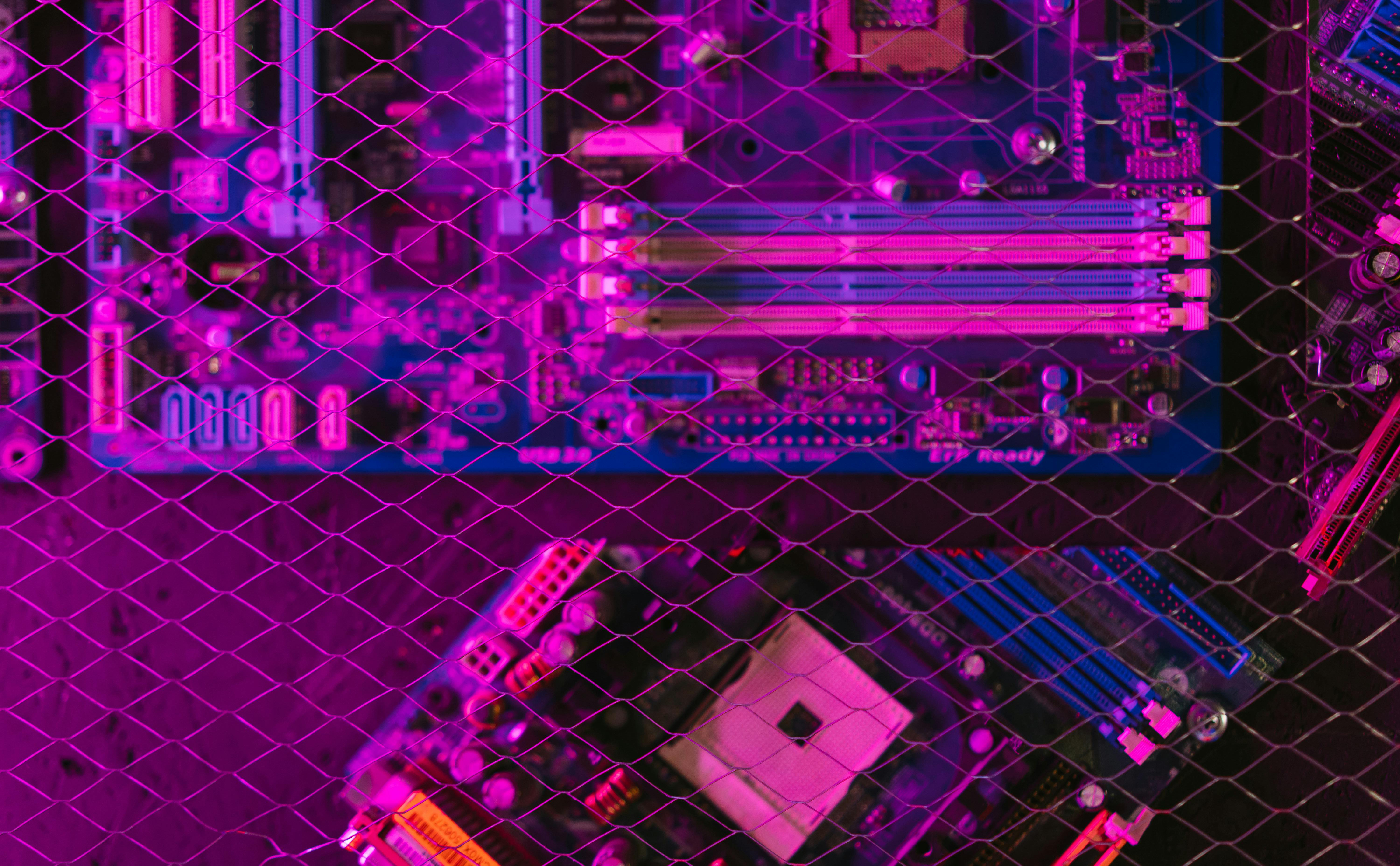 A pink and blue circuit board behind a wire mesh and viewed from above.