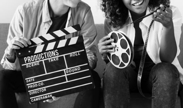 Black and white picture of 2 people holding a clapper board and a film reel