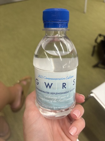 Hand holding a small clear water bottle with a blue cap and a commemorative “GWRS” label.