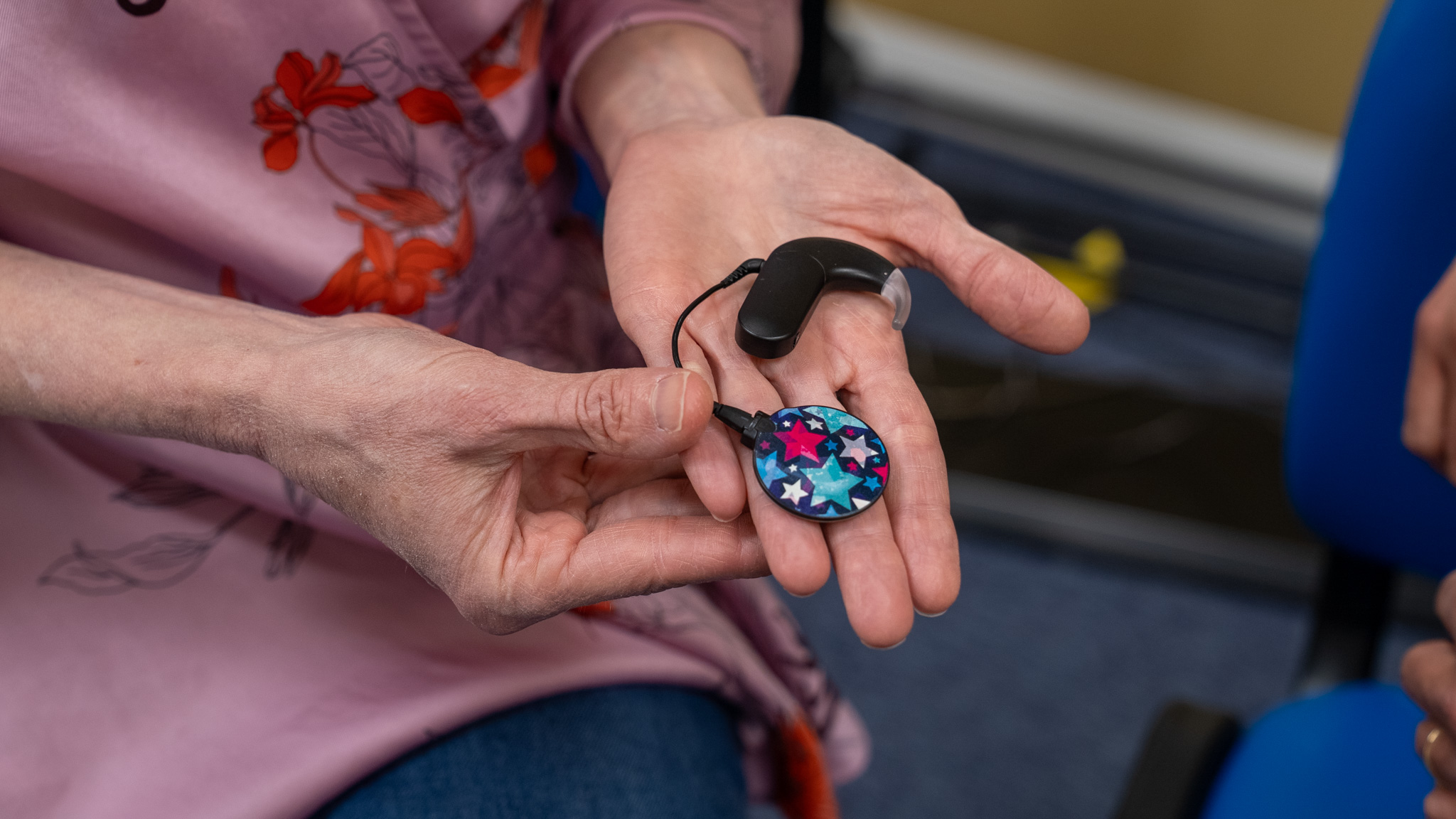 An outstretched hand holds a plastic device which is mainly black but has a colourful circular part 