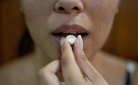 Woman holding white pill in front of her mouth about to swallow