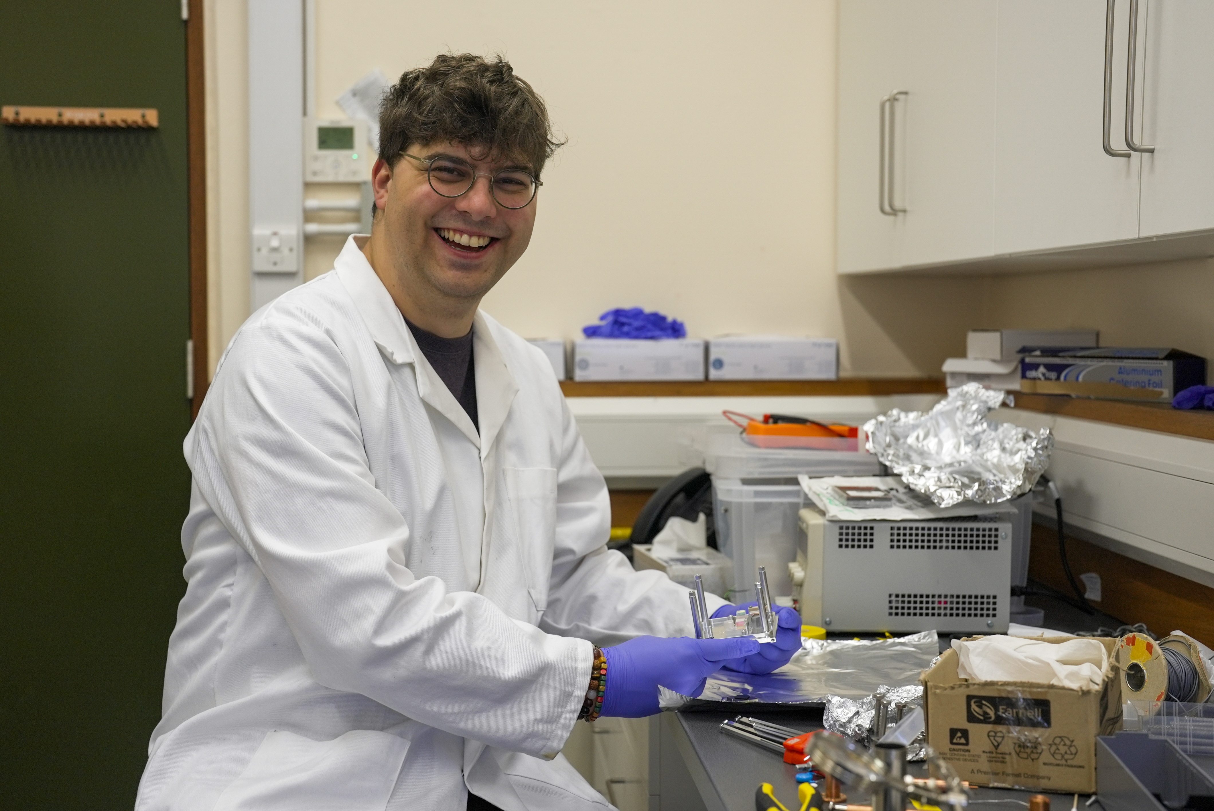 Physicist Tim Fuchs in white lab coat holding his experimental dark matter device