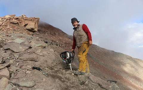 Man stood on a remote rockside holding a large drill