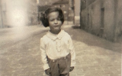 Black and white image of a young boy wearing a shirt and shorts, standing in a cobbled street.