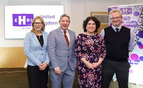 Four people, two women and two men, stood indoors in front of a screen and pop-up banner advertising EHRI, the European Holocaust Research Infrastructure 