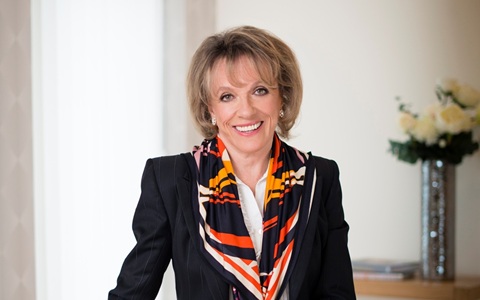 Head and shoulders photo of a woman with light coloured shoulder length hair smiling, she is wearing a dark coloured blazer and bright patterned scarf