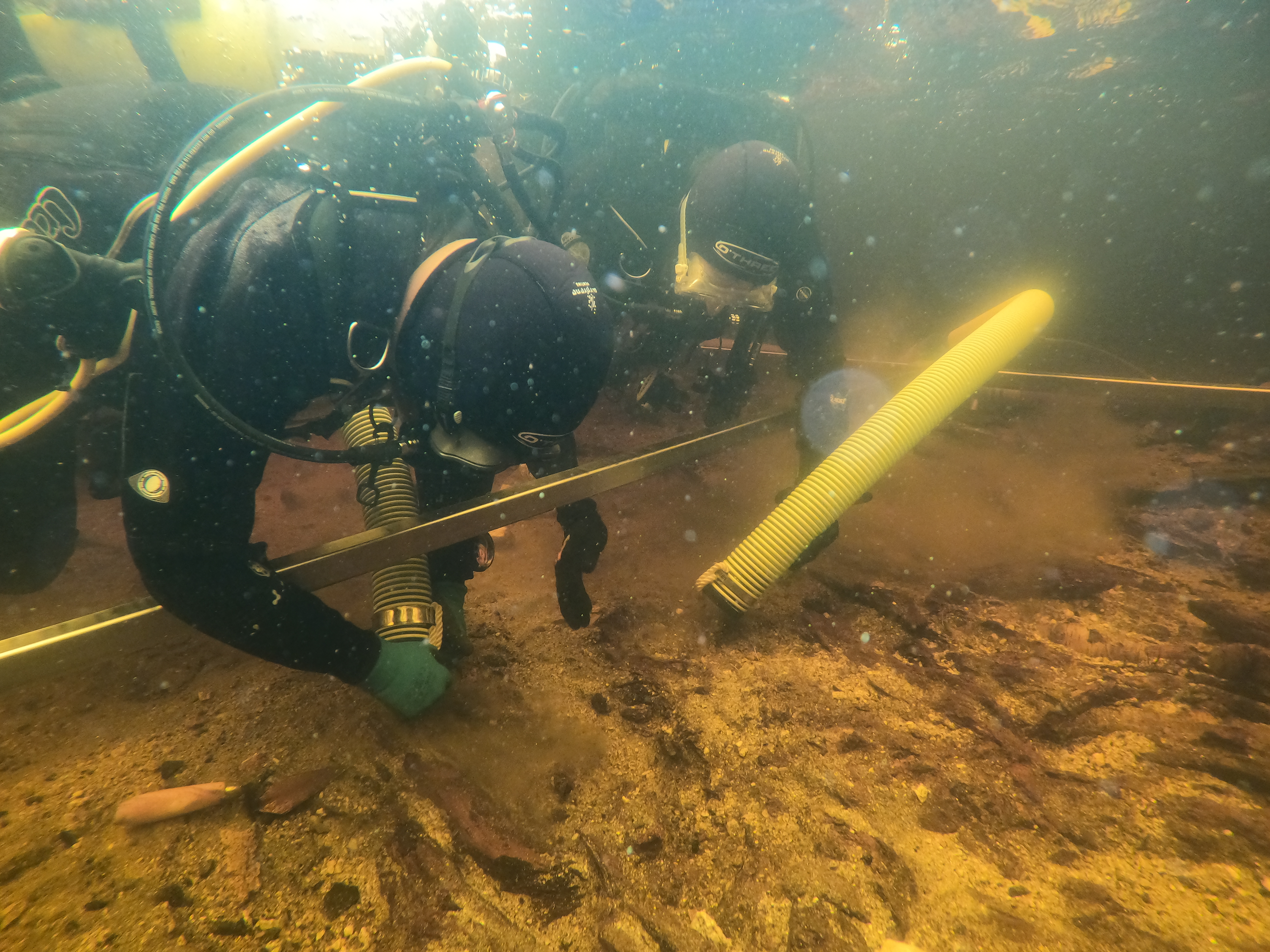 A diver excavating a loch bed, underwater, wearing a yellow oxygen tank.