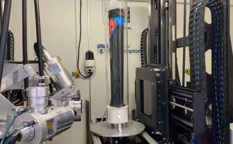 A black tower of material inside a clear tube, surrounded by large scanning equipment