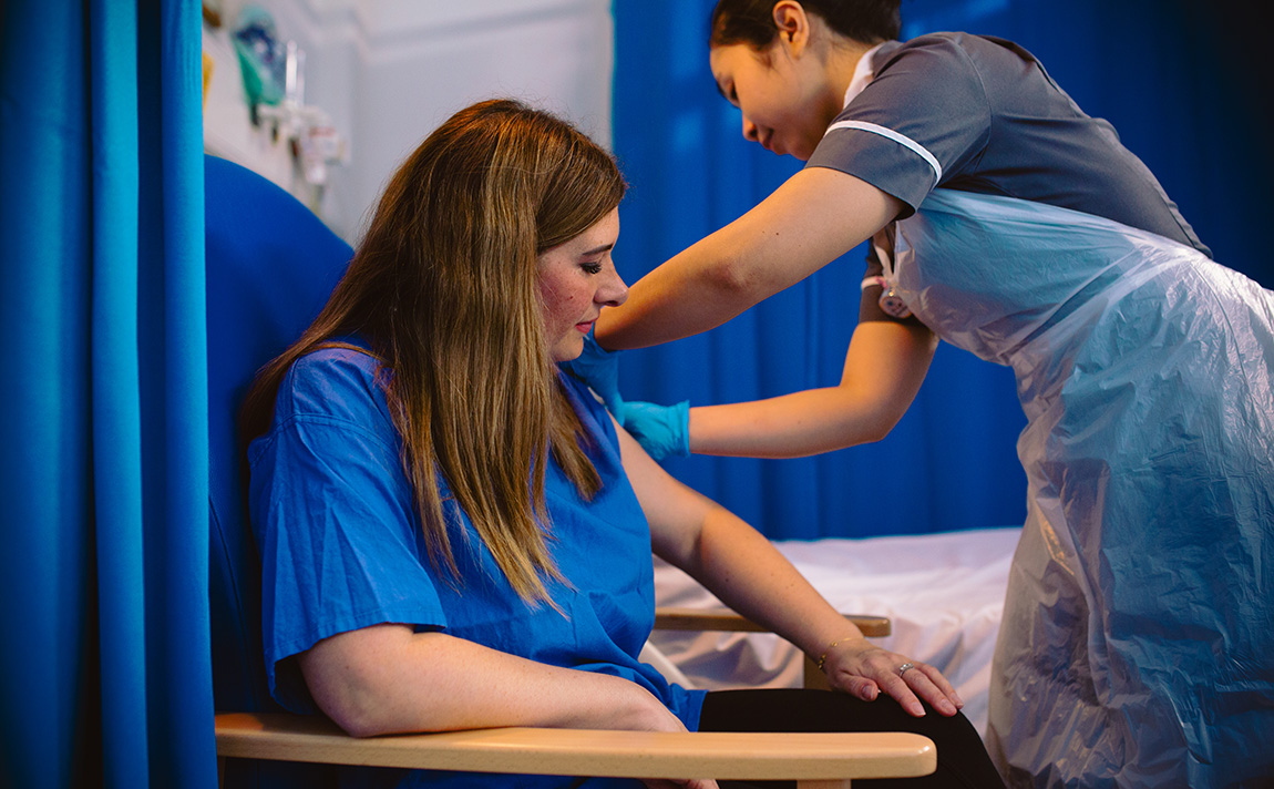 Woman nurse leaning over a woman patient to give her an injection.